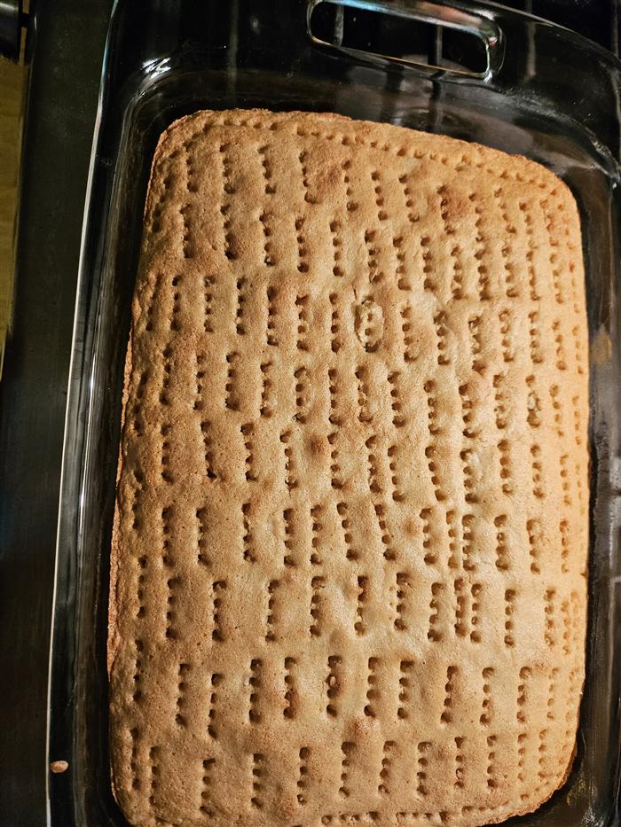 A baked tres leches sponge in a glass baking dish, its whole surface poked with neat rows of fork holes.